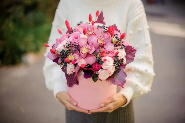Arranjo de flores de fowers rosa em caixa redonda rosa nas mãos de mulher jovem — Fotografia de Stock