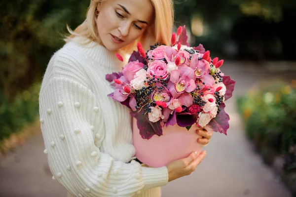 Hermosa mujer cuidadosamente sostiene caja redonda rosa con flores en el interior — Foto de Stock