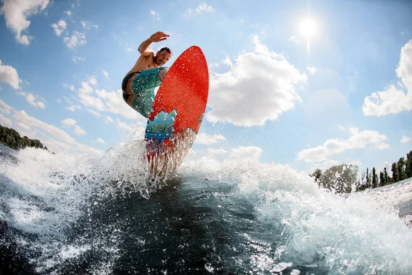 Hombre activo saltando sobre el wakeboard brillante abajo del río contra el fondo del cielo — Foto de Stock