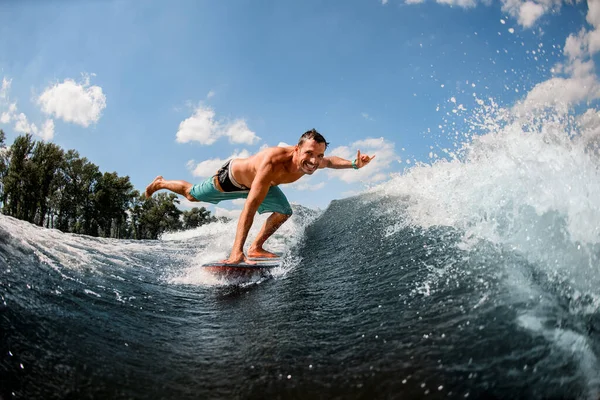 Glücklicher Mann steht auf Surfbrett gestützt auf ein Bein und einen Arm — Stockfoto