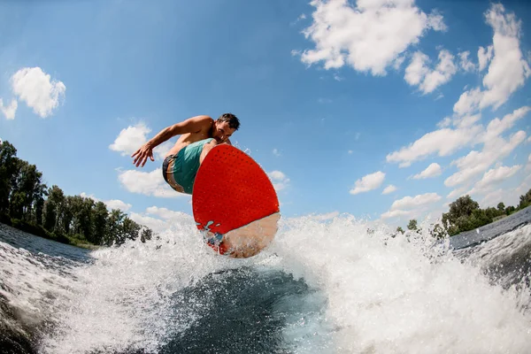 Vuxen man vaknar hoppar på en våg på en ljus surfbräda — Stockfoto