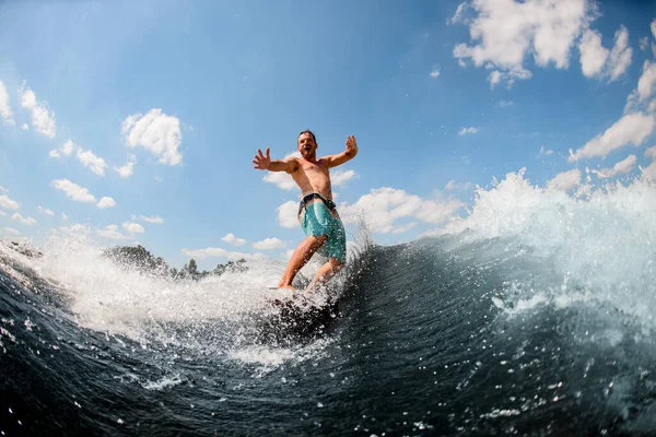 Emotionaler erwachsener Kerl reitet aktiv auf den Wellen auf dem Surfbrett vor blauem Himmel — Stockfoto