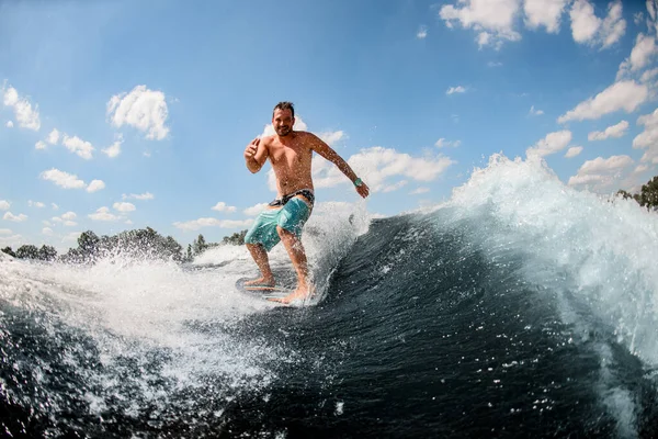 Sportlicher Typ reitet aktiv auf den Wellen auf dem Surfbrett vor blauem Himmel — Stockfoto