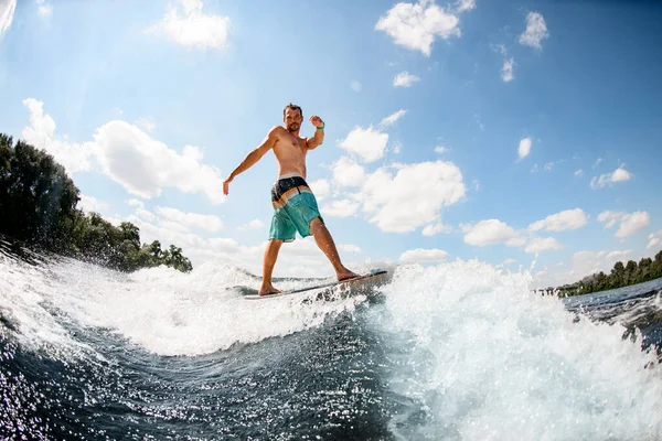 Atraente masculino wakesurfer balanceamento a bordo na onda contra o céu azul — Fotografia de Stock