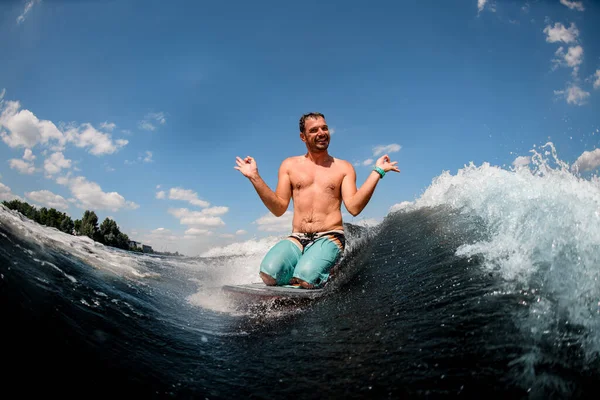Fröhlicher Mann sitzt auf Surfbrett und zeigt eine Geste mit den Händen — Stockfoto