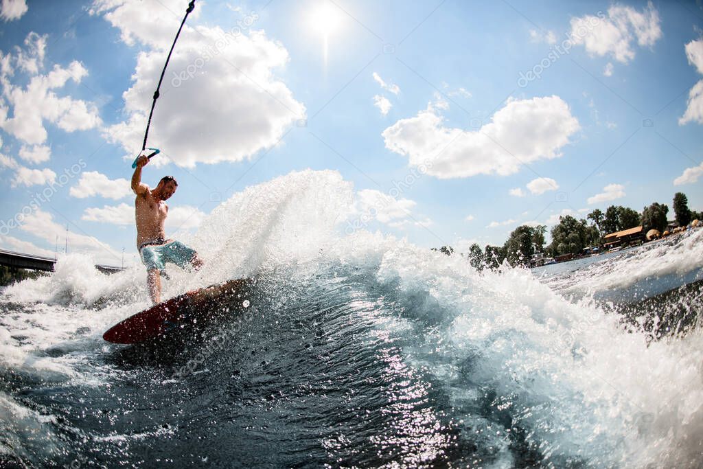 Adult handsome man wakesurfing on the river and pulled by a boat.