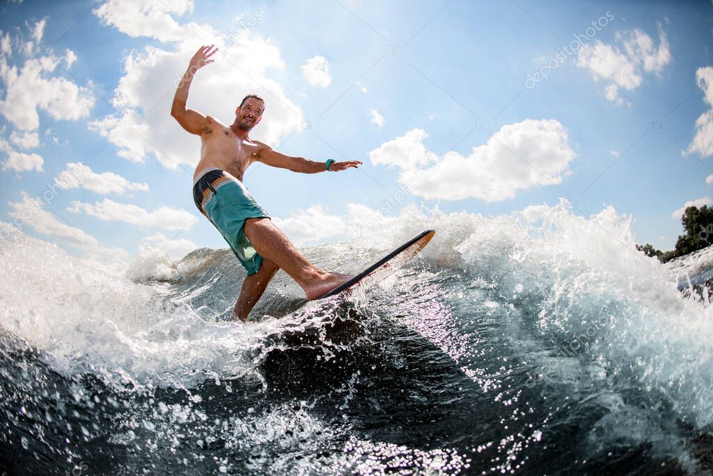 active guy wakesurfing on the board down the river against the background of sky