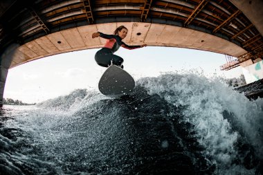 Dalgıç kıyafetli genç bir dişi sörf tahtasında sörf yapıyor..