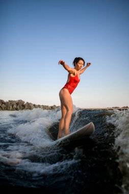 woman in red swimsuit balanced on surfboard and rides on the wave. clipart