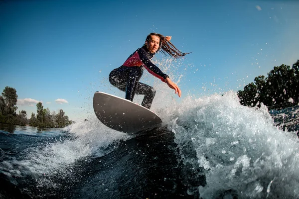 young female sportsman actively rides the splashed wave on surfboard