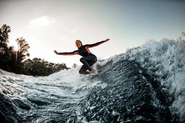 Aktive junge Frau balanciert im Neoprenanzug auf Surfbrett und reitet auf der Welle. — Stockfoto