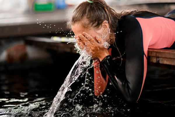 Giovane donna che indossa muta lava il viso con acqua e spruzzi e goccioline d'acqua intorno a lei — Foto Stock