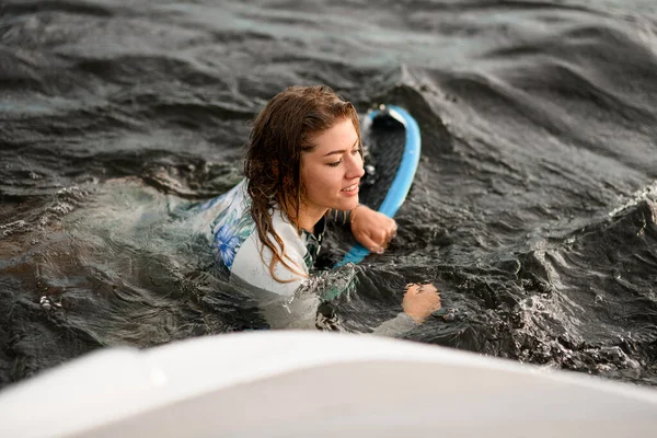 Jeune femme aux cheveux bruns nage dans l'eau avec planche de surf — Photo