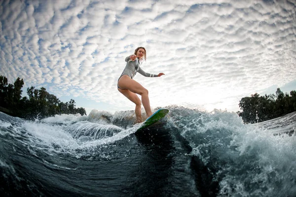 Genç, güzel sarışın kadın sörf tahtasında bulutlu arka planda dalgalanır. — Stok fotoğraf