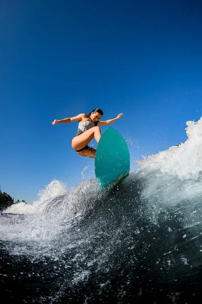 Vista de mulher desportiva em maiô cinza que salta com placa de surf brilhante . — Fotografia de Stock
