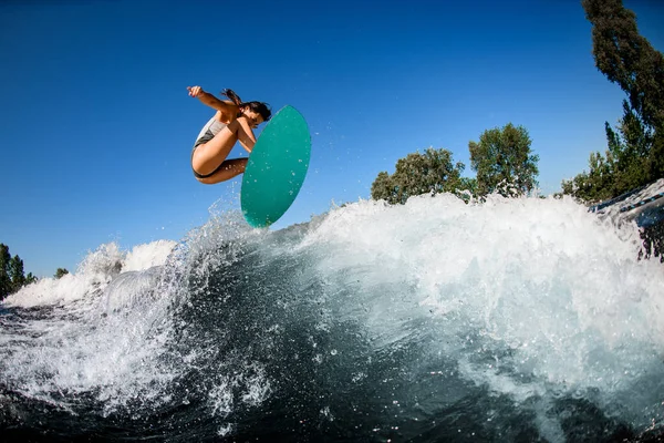 Mujer activa wakesurfer en traje de baño gris salta con tabla de surf brillante —  Fotos de Stock