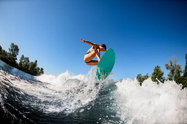Frau im grauen Badeanzug springt mit hellem Surfbrett — Stockfoto