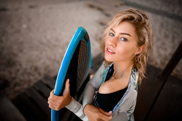 Hochwinkelaufnahme einer Frau, die ihr Surfbrett hält und ihren Neoprenanzug auszieht — Stockfoto