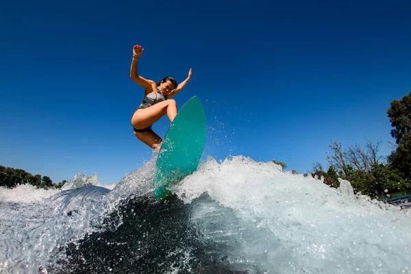 Desportivo ativo mulher wakesurfer em saltos maiô cinza com placa de surf brilhante — Fotografia de Stock