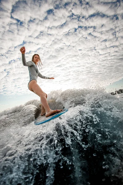 Mulher com cabelo molhado desce a onda na prancha de surf contra fundo céu nublado — Fotografia de Stock