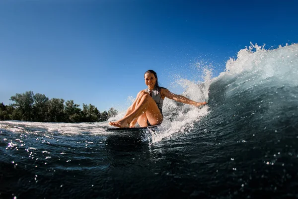 幸せな女性はウェイクサーフボードに座って波に乗り片手で波に触れる — ストック写真