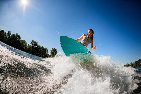 Vista di atleta donna in costume da bagno grigio che salta con tavola da surf luminoso. — Foto Stock