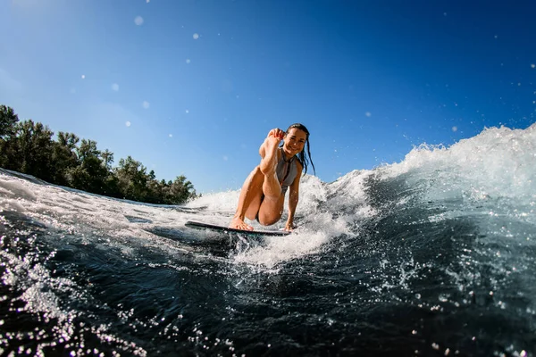 Allegra giovane donna siede su tavola da surf con la gamba tesa — Foto Stock