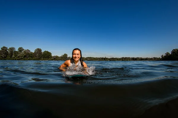 Mujer joven con el pelo castaño flota en el río en tabla wakesurf —  Fotos de Stock