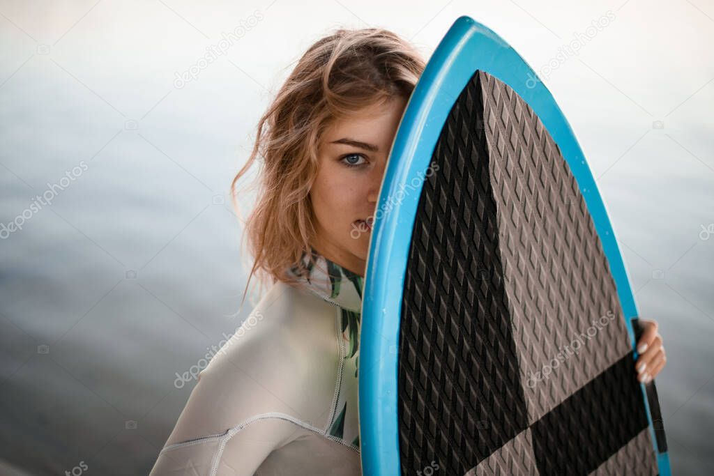 portrait of young beautiful blonde woman with wet hair which covering her face with wakesurf board