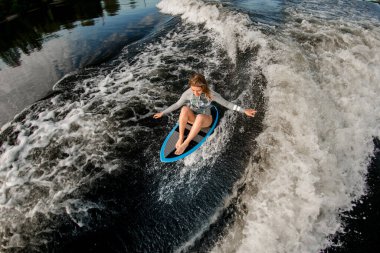 top view of blond woman who riding the waves while sitting on wakesurf board clipart