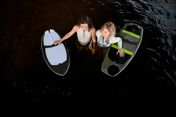 Vista de ángulo alto de hermosas mujeres en trajes de baño que se paran en el agua con tablas de surf cerca —  Fotos de Stock