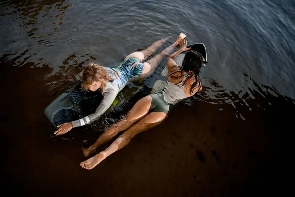 Vista superior de dos mujeres nadando en diferentes direcciones en el agua en sus tablas de surf —  Fotos de Stock