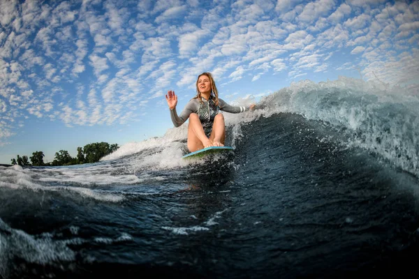 Mulher senta-se no wakesurf bordo e monta a onda e toca as ondas com uma mão — Fotografia de Stock