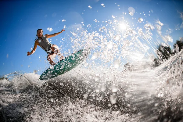 Hermosa vista de atleta mujer en traje de baño gris que salta con tabla de surf brillante. —  Fotos de Stock