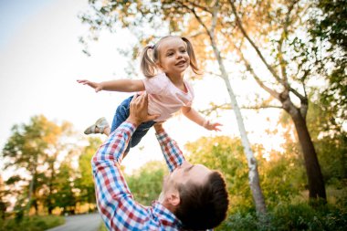 Genç baba, yakışıklı kızını elleriyle yükseğe kaldırır.