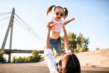 Genç anne, ellerini havaya kaldırarak kızını büyütüyor.