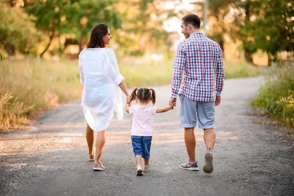 Πίσω όψη του ευτυχισμένου οικογενειακού ζευγαριού που περπατά με το παιδί κρατώντας τα χέρια της σε ηλιόλουστη μέρα του καλοκαιριού — Φωτογραφία Αρχείου