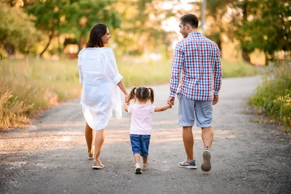 Achteraanzicht van gelukkig familie paar die loopt met kind houdt haar handen op zonnige zomerdag — Stockfoto