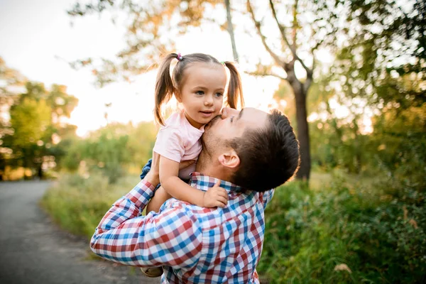 Jonge vader houdt zijn kleine lieve dochter in zijn armen en kust haar. — Stockfoto