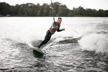 Siyah mayo giymiş kaslı bir adam su kayığıyla dalgaların arasından geçiyor.