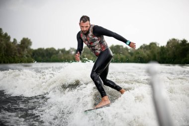Siyah mayo giyen ıslak adam su kayığıyla dalgaların arasından geçiyor.