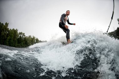 Vahşi sporcu sörf tahtasına biniyor teknenin arkasındaki dalgalarda.