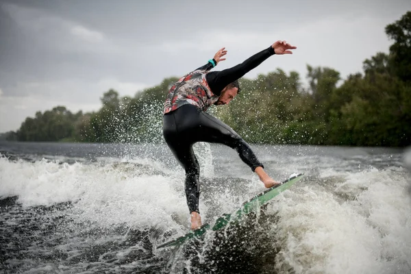 Sportig man i våta svarta badkläder försöker balansera på vågen — Stockfoto
