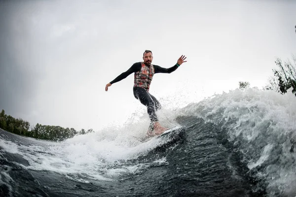 Aktiver Mann im schwarzen Badeanzug reitet auf Wasserbrett durch die Wellen — Stockfoto