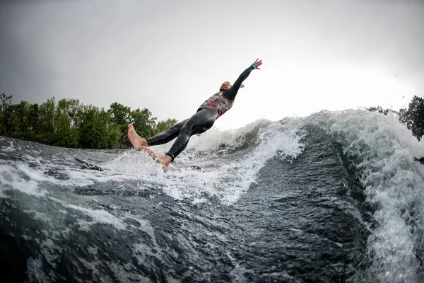 Man i svart baddräkt faller från surfbräda i floden vatten. — Stockfoto