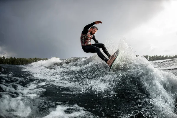 Energetischer Sportler reitet mit seinem Surfbrett auf einer Welle. — Stockfoto