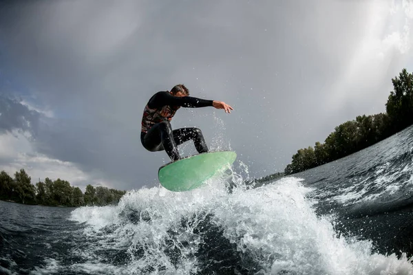 Deportista enérgico salta sobre la ola con su tabla de surf. —  Fotos de Stock