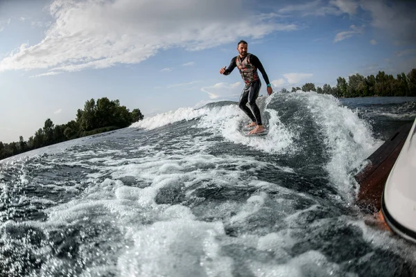 Leende kille rider surfbräda på vågorna bakom båten. — Stockfoto