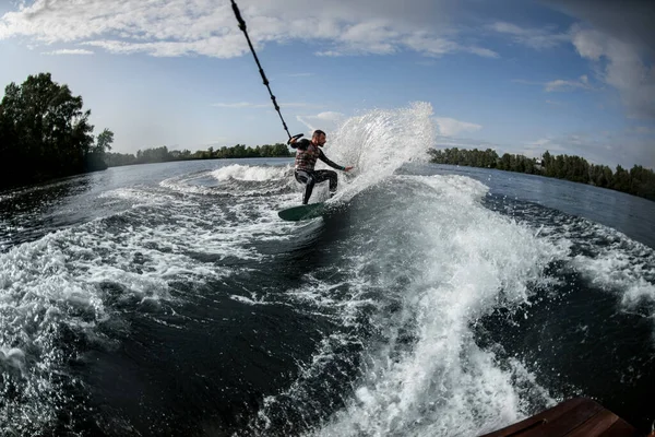 Sportif homme tient tendue corde de bateau à moteur et promenades sur wakeboard sur l'eau de la rivière — Photo