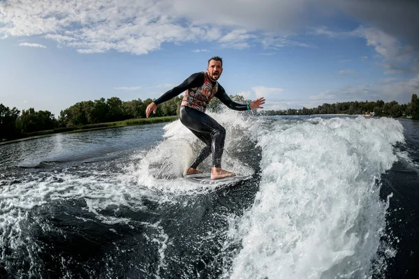 Attraktiv man svart baddräkt rider en våg utanför kusten med sin surfbräda. — Stockfoto